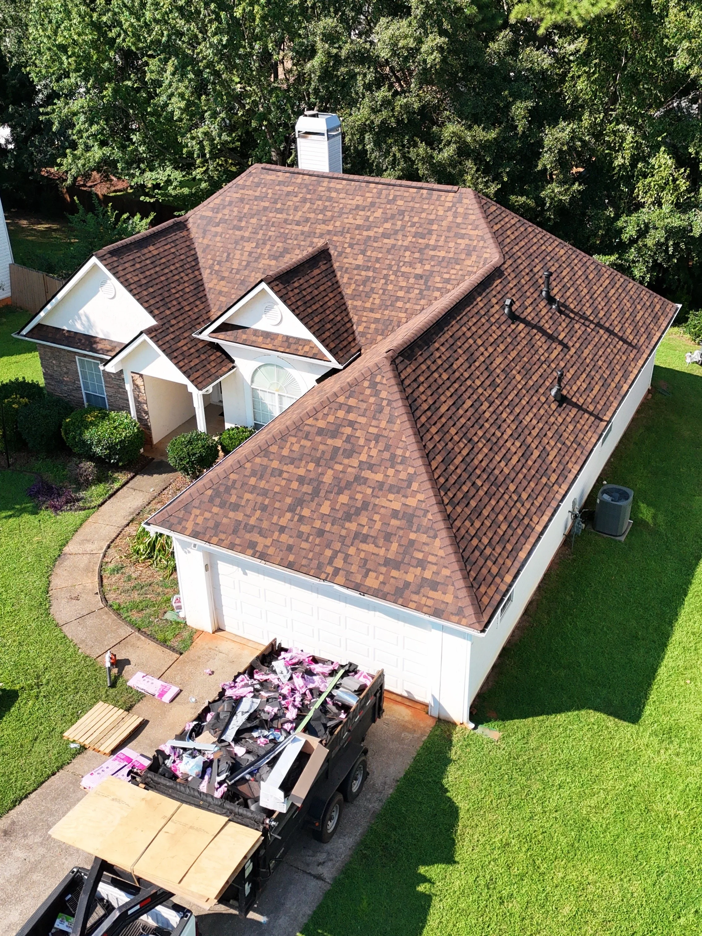 A house with a tiled roof seen from above, along with a large dumpster full of debris and building materials, indicating ongoing construction or renovation work.